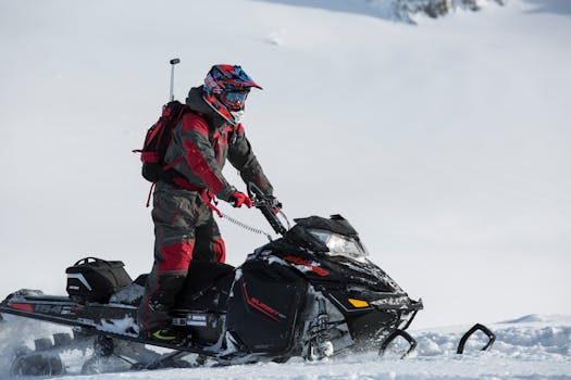 Snowmobiler navigating snowy terrain wearing protective gear and helmet.